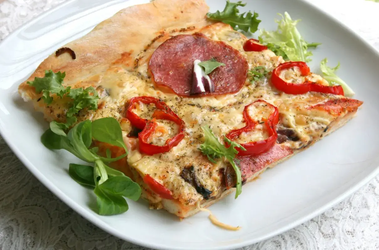 Pyszne ciasto na pizzę z salami, papryką i serem, ozdobione świeżymi ziołami.