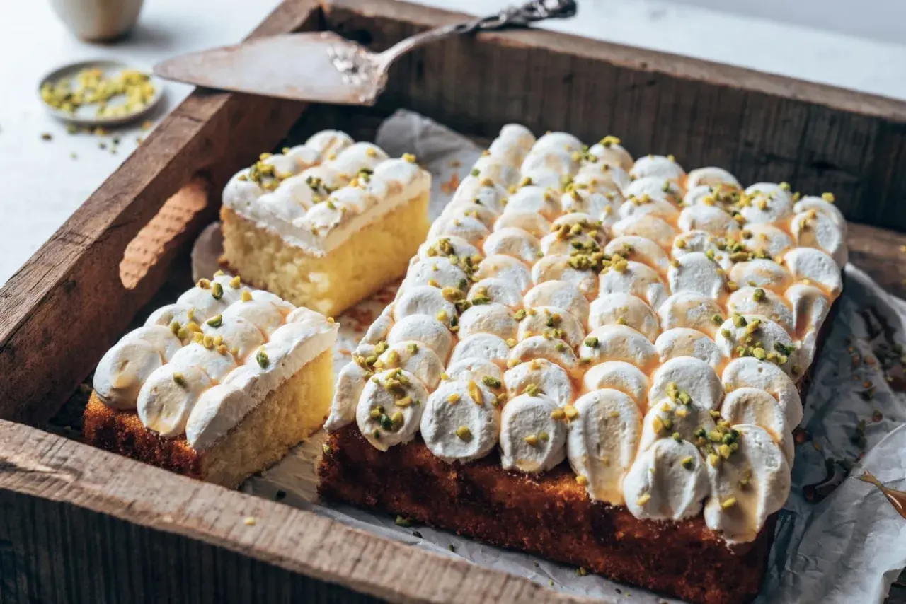 Ein köstlicher Joghurt Kuchen mit luftiger Creme und gehackten Pistazien, serviert auf einer rustikalen Holzschale.