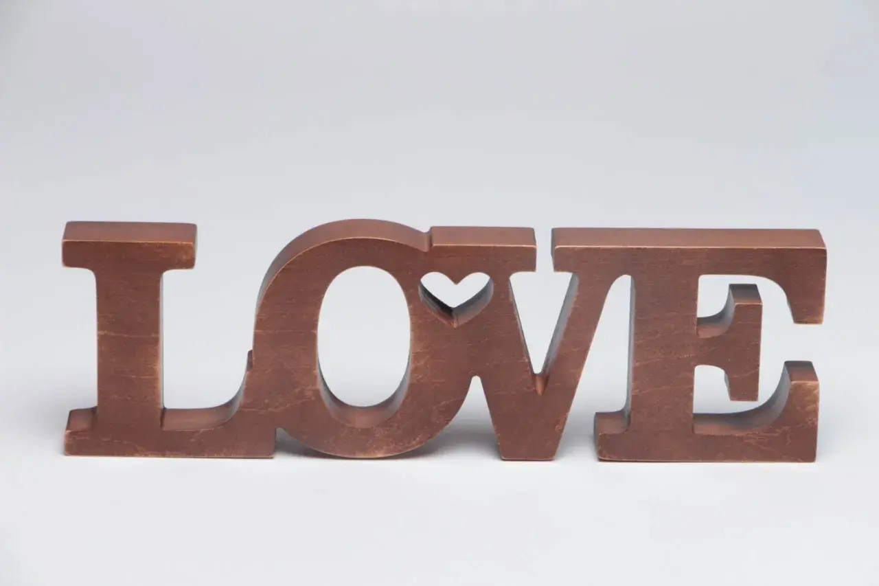Letras de madera marrón forman la palabra "LOVE", con un corazón tallado en la "O".