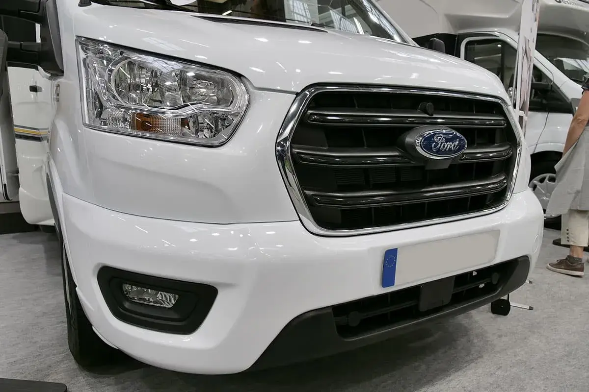 Avant d'un camping-car blanc avec le logo Ford. Ce véhicule est équipé d'un moteur Ford 2.2 TDCI, parfait pour vos voyages.