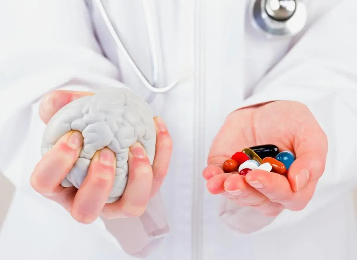 Mains tenant un cerveau en plastique et une poignée de pilules colorées, symbolisant la recherche sur la maladie de Parkinson, dernière découverte.