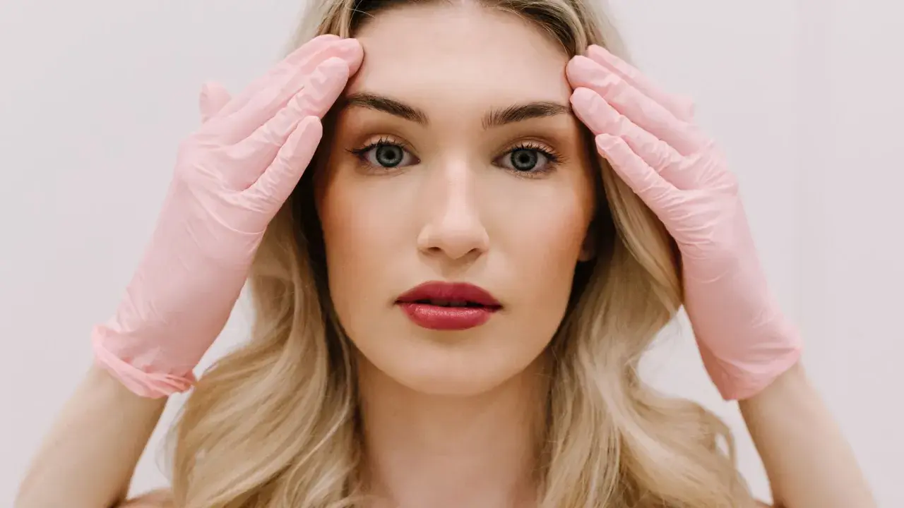 Kobieta w różowych rękawiczkach dotyka skroni, przygotowując się do zabiegu face lifting.
