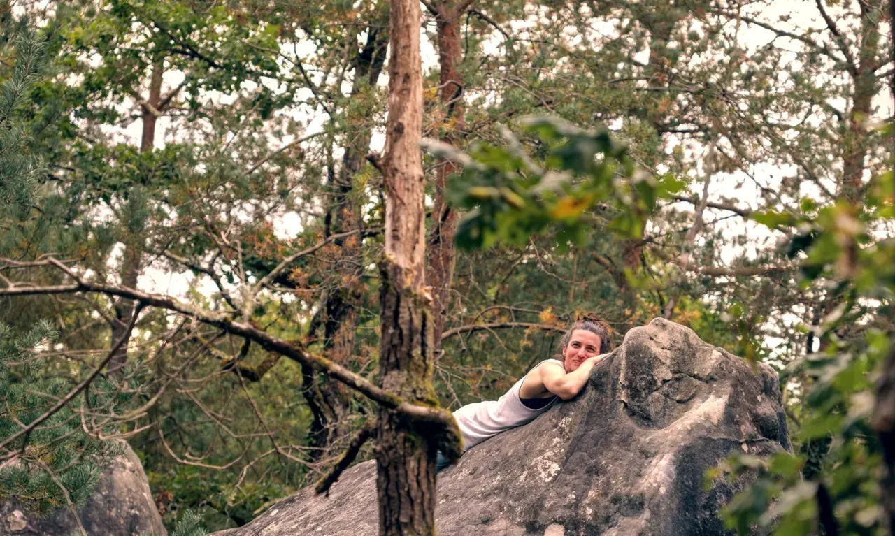 Frau ruht auf einem großen Fontainebleau Boulder im Wald, umgeben von Bäumen.