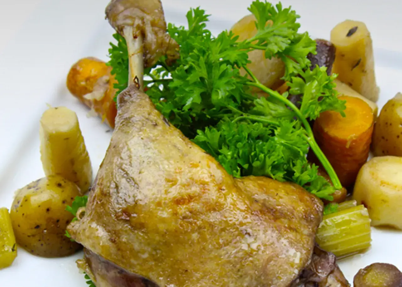 Une savoureuse cuisse de canard confite, accompagnée de pommes de terre et de carottes rôties, garnie de persil frais.
