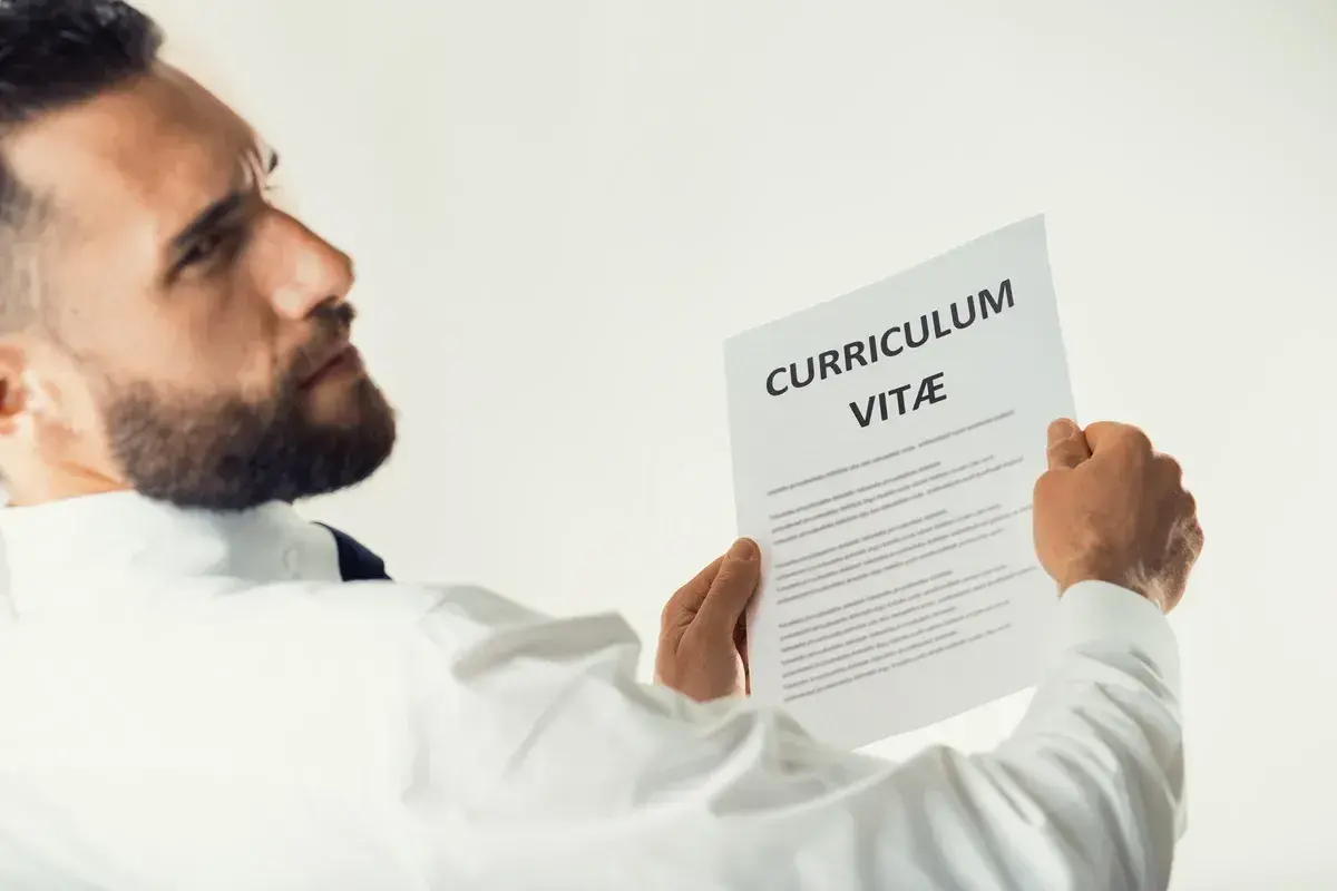 Mężczyzna w białej koszuli analizuje CV, szukając kluczowych kompetencji.