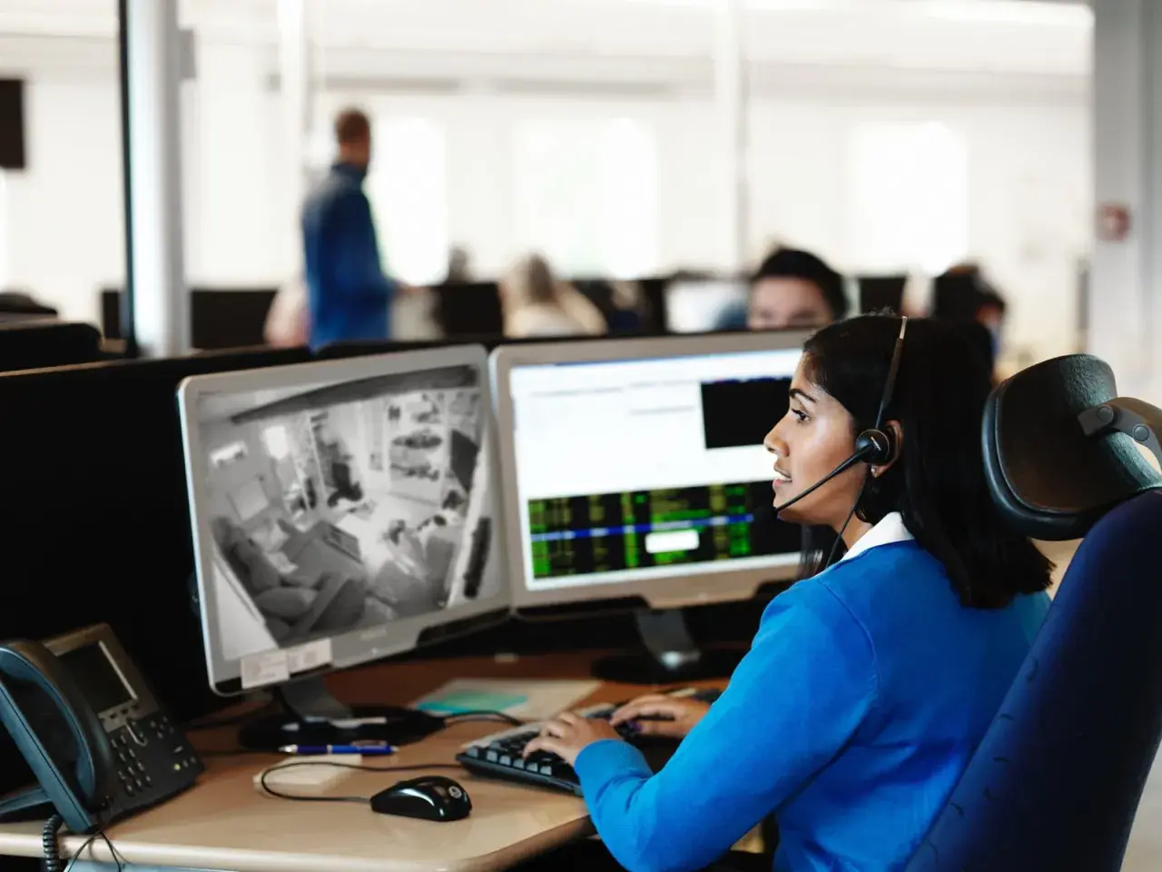 Kvinna med headset övervakar kameror på en arbetsplats, följer brandrutiner.