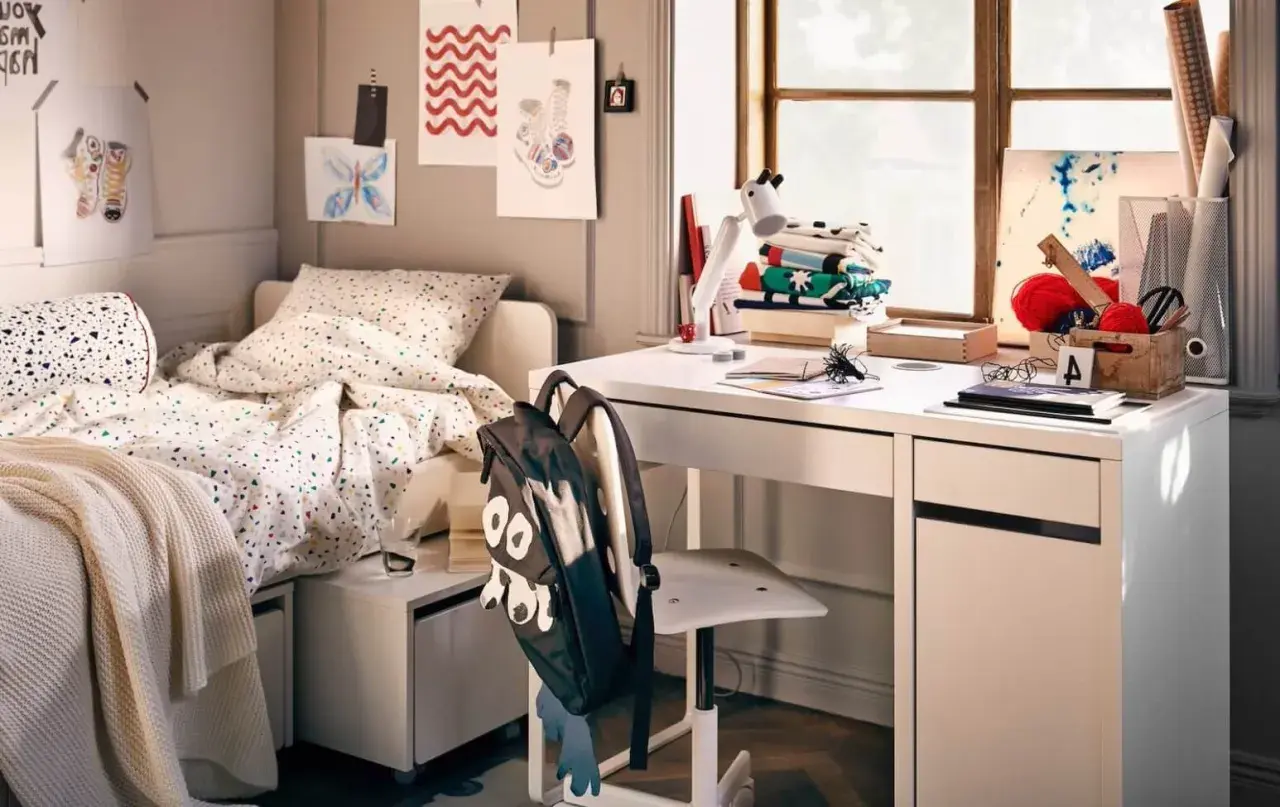 Aménagement petite chambre ado : lit confortable, bureau blanc avec fournitures créatives, et un sac à dos rigolo.