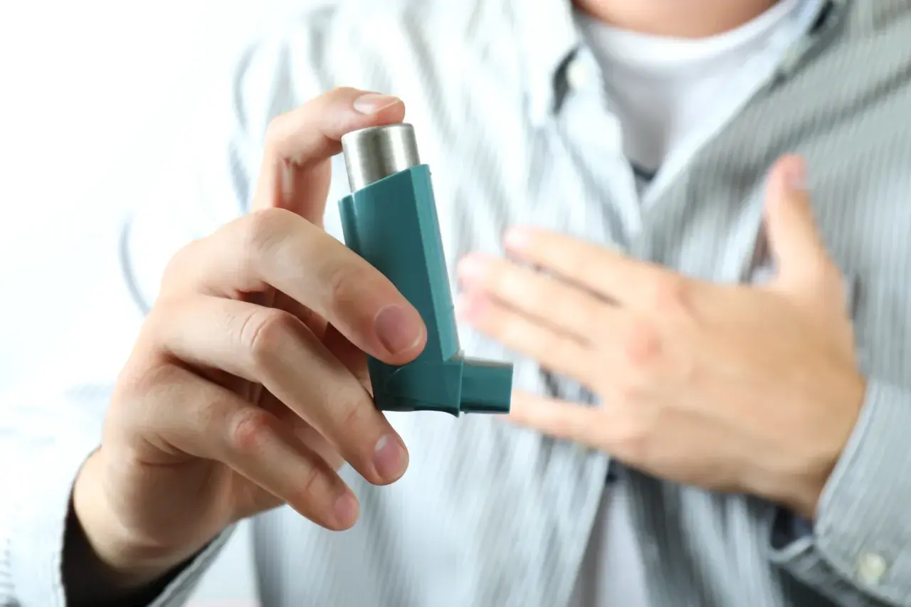Dłoń trzymająca inhalator, druga ręka na piersi. To obraz walki z astmą, sensu stricto.