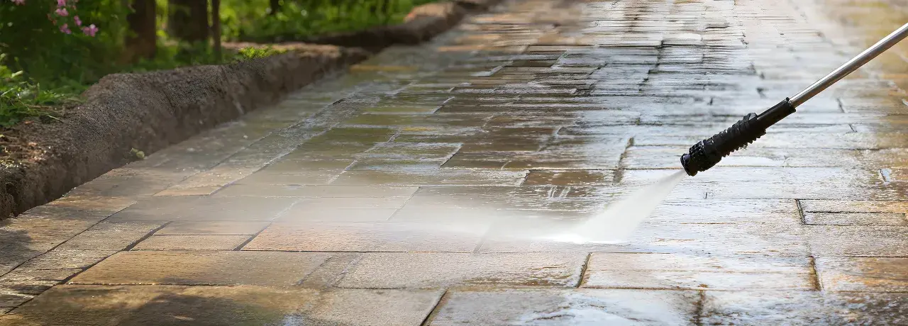 Hochdruckreiniger säubert ein Betonpflaster. Der Wasserstrahl entfernt Schmutz und lässt die Steine wieder wie neu aussehen.