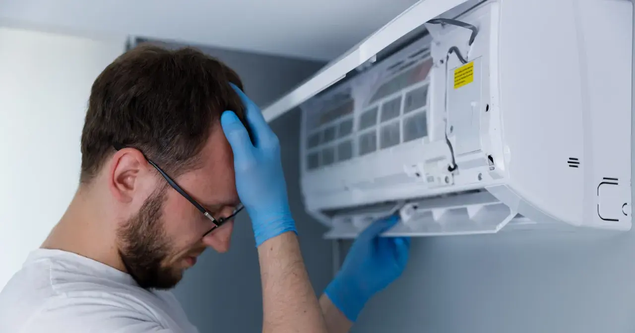 Mężczyzna w niebieskich rękawiczkach sprawdza klimatyzator.