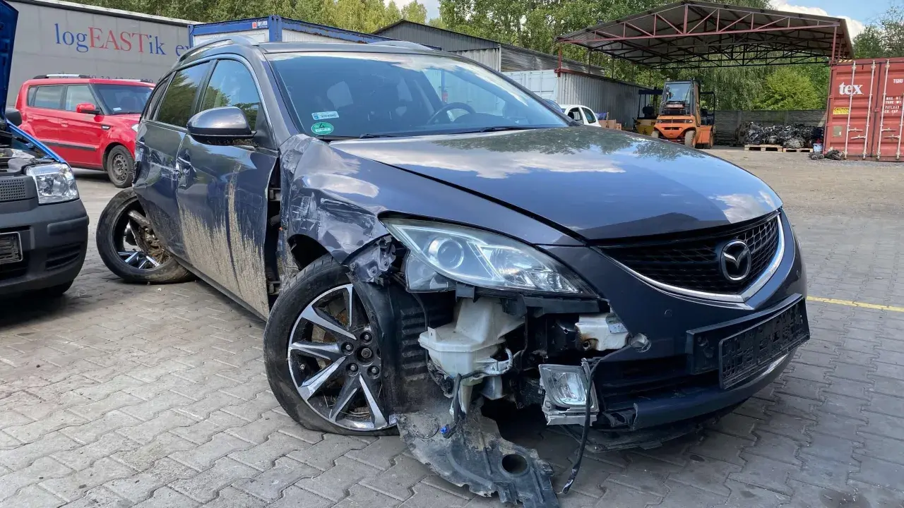 Uszkodzona Mazda na złomowisku, z urwanym zderzakiem i przebitą oponą. Może to być początek procesu, jak zezłomować samochód.