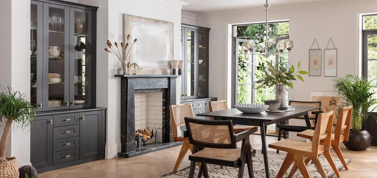 Modern dining room with dark grey cabinets, marble fireplace, and a dark wood table with cane-backed chairs, showcasing current trends in dining room furniture.