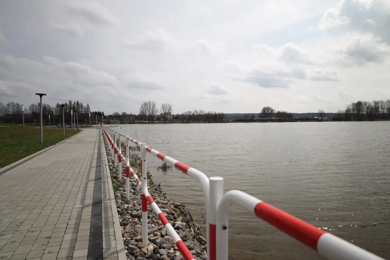 Spacerem nad zalewem wolbromskim, z czerwono-białą barierką i brukowaną ścieżką.