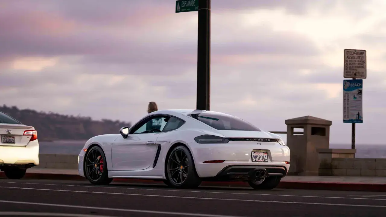 Białe Porsche GT4 z czerwonymi zaciskami hamulcowymi stoi przy drodze z widokiem na ocean.