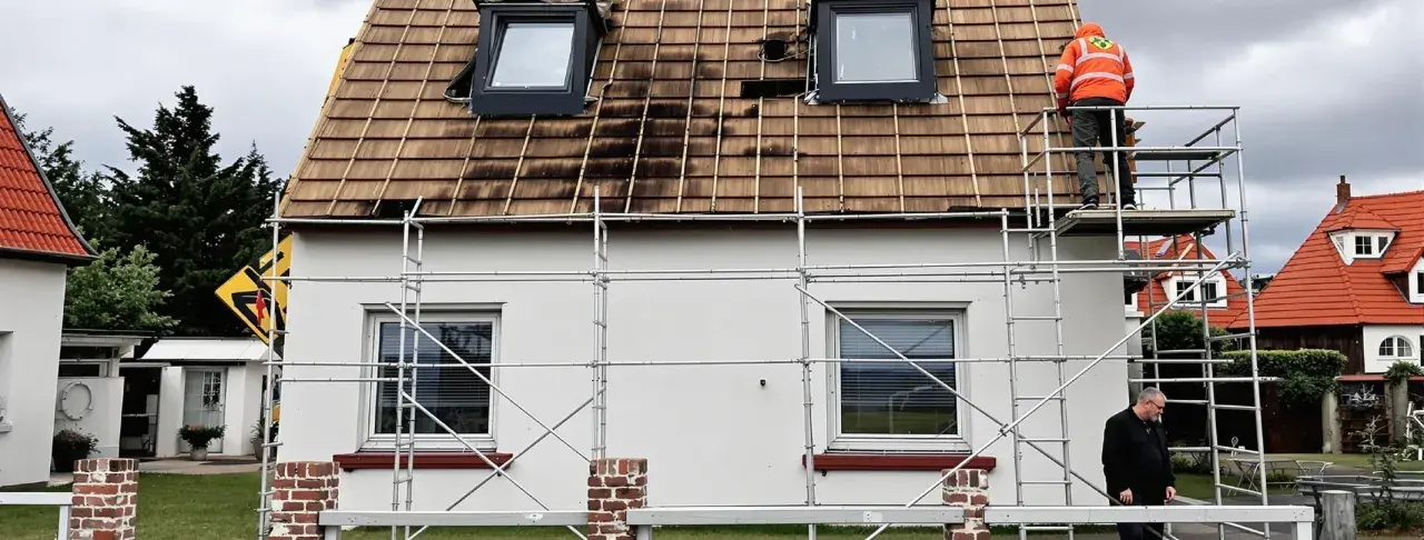 Gerüst am Haus, Dach wird saniert. Ein Arbeiter in Warnweste prüft die Arbeiten. Wer kontrolliert Sanierungspflicht?