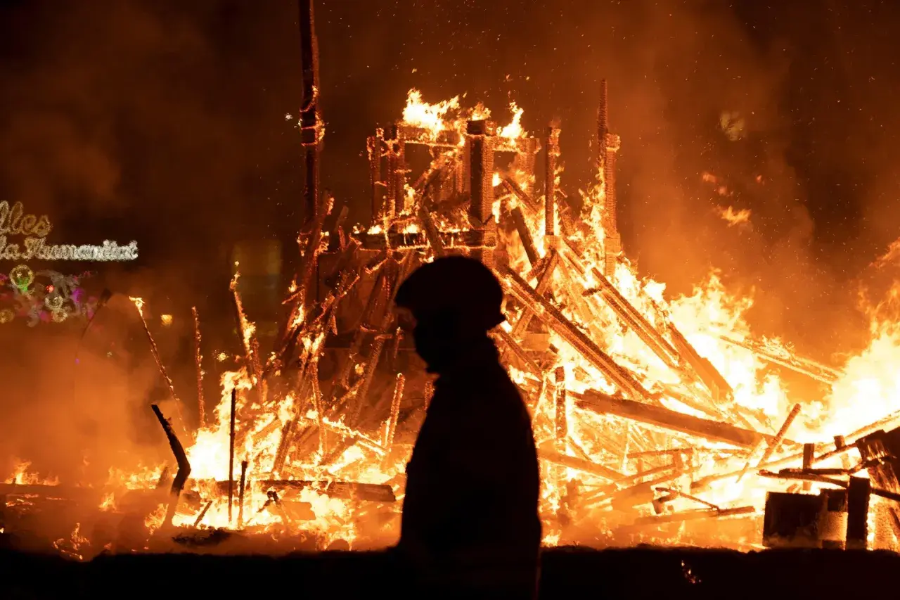 Silueta de persona observando la **cremà** de una falla en **Valencia**. El fuego consume la estructura de madera, creando un espectáculo de llamas y humo.