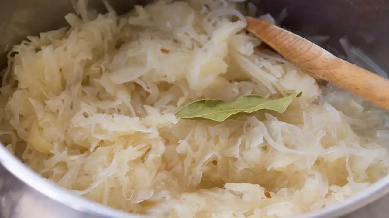 Frisch zubereitetes Sauerkraut mit Lorbeerblatt und einem Holzlöffel. Perfekt als Beilage zu einem herzhaften Gericht, vielleicht mit einem Glas Wein.