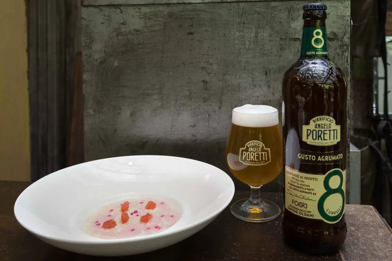 Un bicchiere e una bottiglia di birra Angelo Poretti, una brown ale dal gusto agrumato, accanto a una ciotola con un piatto rosa e pezzetti rossi.
