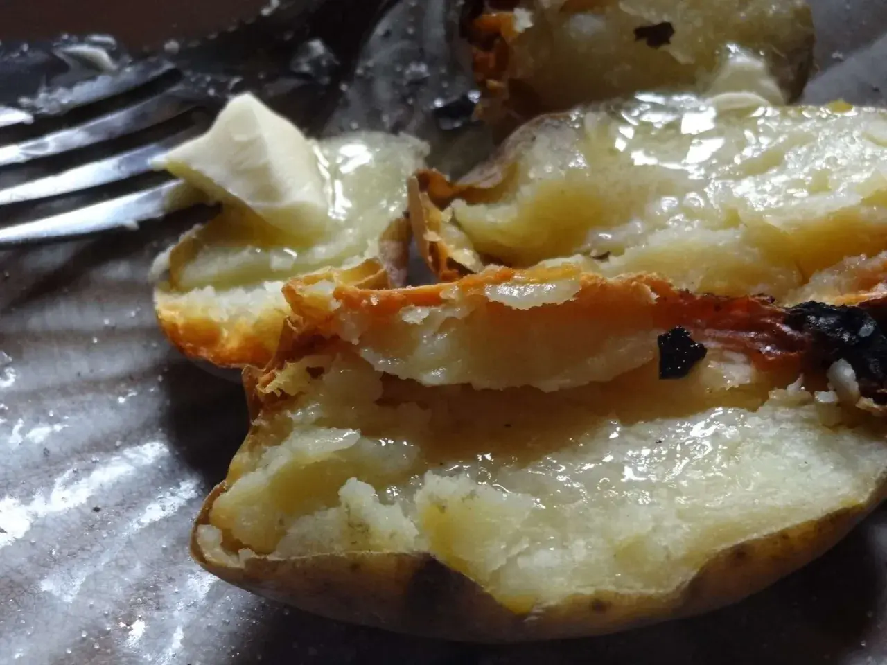 Pommes de terre cuites dans la cendre, ouvertes et garnies de beurre fondant. Un délice simple.