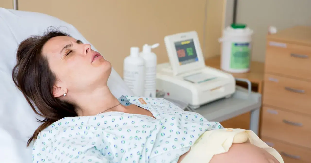 Kobieta w szpitalnym łóżku, monitor KTG, butelki z płynem. Badanie może wykluczyć obecność bakterii Streptococcus agalactiae.