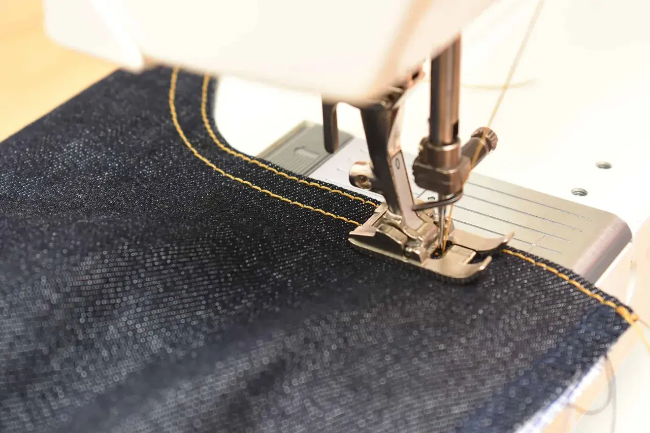 Close-up of a sewing machine stitching dark denim with yellow thread. Perfect sewing machine settings for denim are key for strong seams.