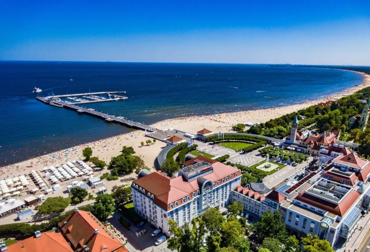 Widok na fajny hotel nad morzem, z plażą pełną ludzi i molo.