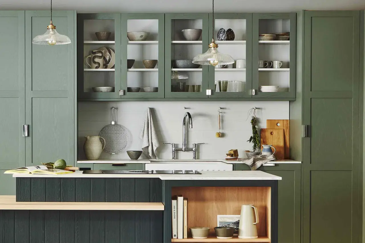 Stylish glass cabinet decor ideas in a modern kitchen with green cabinetry, showcasing ceramic bowls, plates, and glassware.