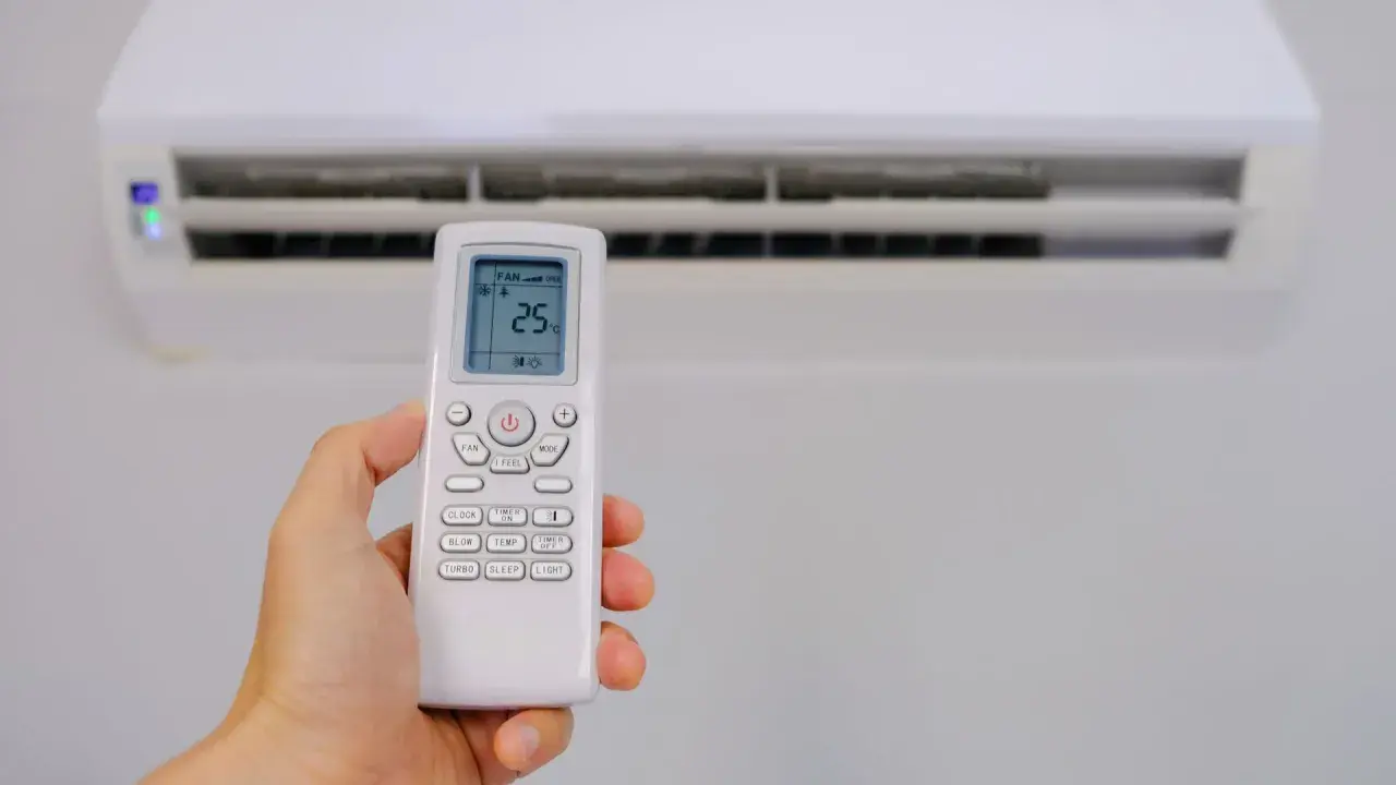 Mano sujetando control remoto de aire acondicionado, mostrando el símbolo deshumidificador aire acondicionado en pantalla.