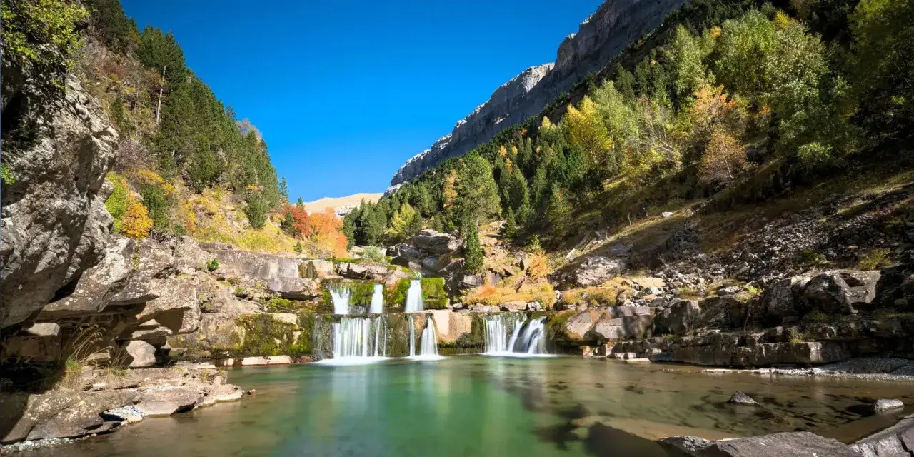Cascada en un valle montañoso con árboles otoñales. Un lugar perfecto para rutas de senderismo inolvidables.
