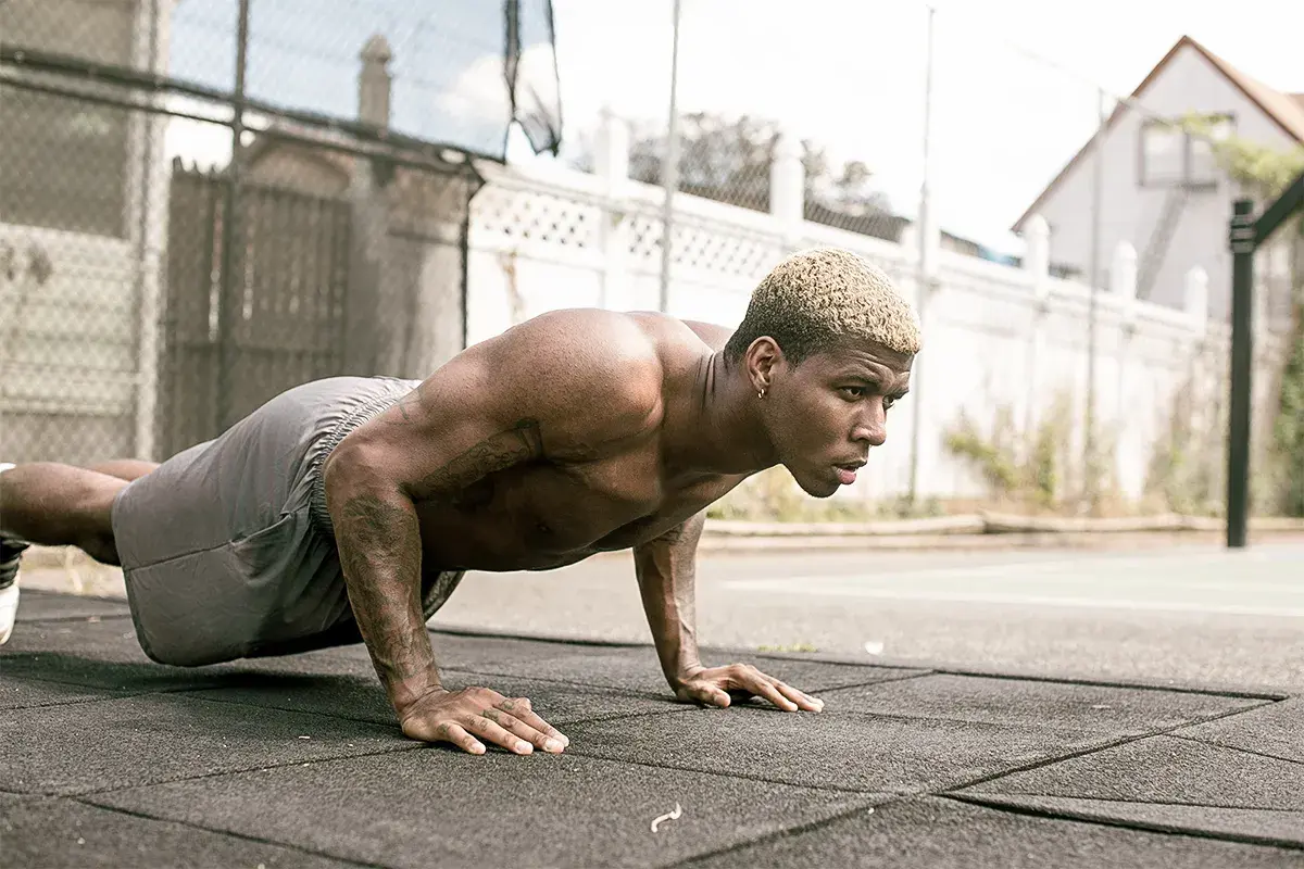 Un homme musclé s'entraîne en extérieur, effectuant des pompes dans un style calisthenics militaire.