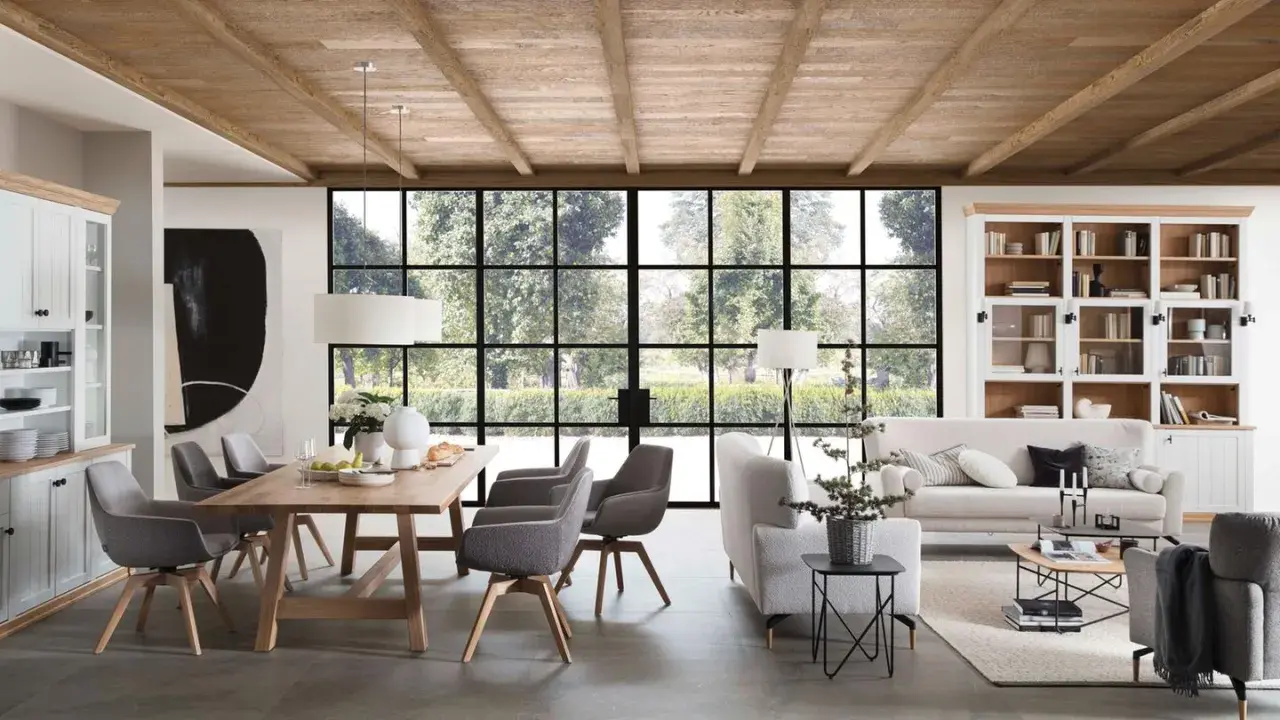 Geräumiges Esszimmer mit Holzbalkendecke im Bauernhaus Stil, Holztisch, grauen Stühlen und großer Fensterfront mit Blick ins Grüne.