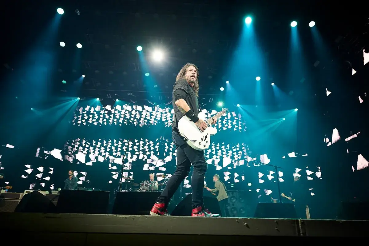 Dave Grohl z Foo Fighters gra na gitarze podczas koncertu, oświetlony niebieskimi światłami. Chce pokazać, jak grać.