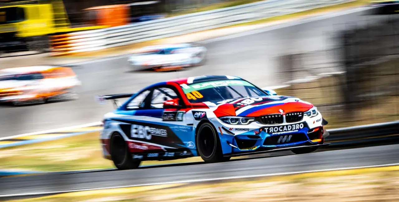Ein BMW GT4-Rennwagen in voller Fahrt, mit lebendigen Farben und Sponsorenlogos, rast auf einer Rennstrecke.