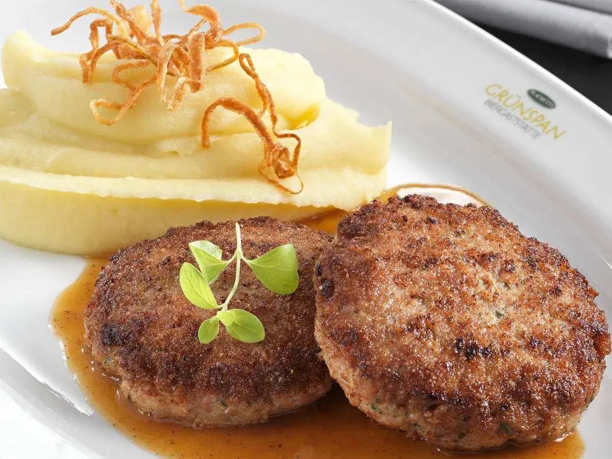 Zwei saftige faschierte Laibchen mit cremigem Kartoffelpüree und knusprigen Röstzwiebeln, garniert mit frischen Kräutern.