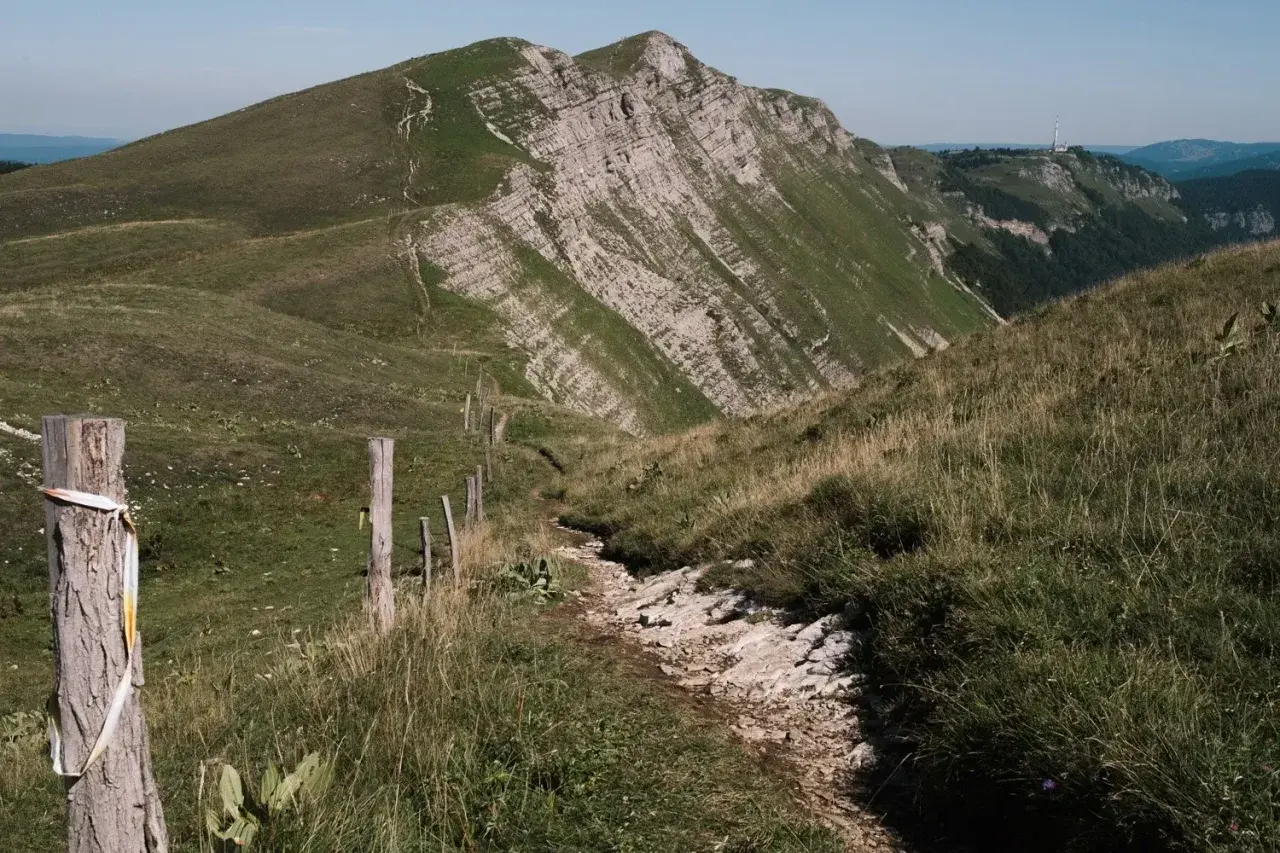 Sentier rocailleux bordé de piquets en bois, menant vers un sommet escarpé. Une invitation à la grande traversée du Jura 7 jours.