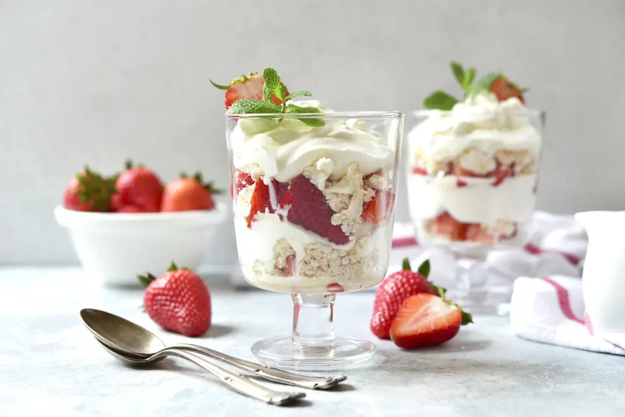 Pyszny Eton Mess z truskawkami i bitą śmietaną w kieliszkach, ozdobiony miętą.