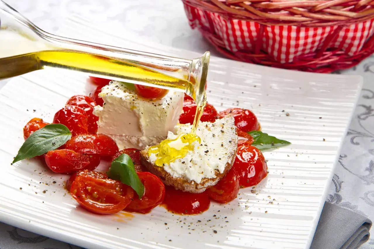 Un piatto di pomodorini confit con robiola, perfetto per un pasto leggero e nutriente in gravidanza. Olio d'oliva versato su una fetta di pane con formaggio.