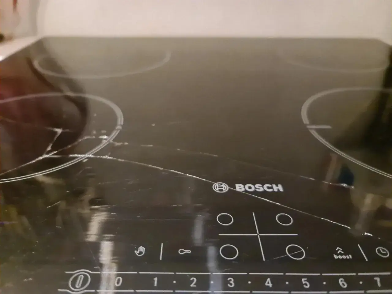 Pęknięta płyta indukcyjna Bosch z widocznymi rysami i pęknięciami na szkle.
