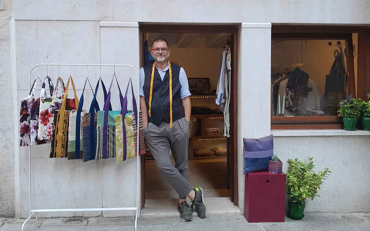 Uomo con metro da sarto nel suo atelier a Venezia. Borse colorate in esposizione.