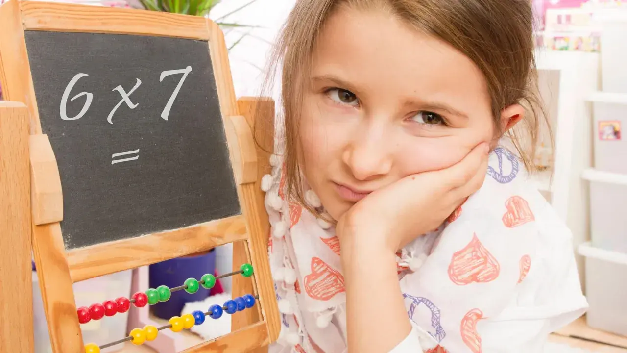Mädchen mit gelangweiltem Gesichtsausdruck vor einer Tafel mit "6x7=". Vielleicht hilft die Trachtenberg-Methode beim Rechnen.