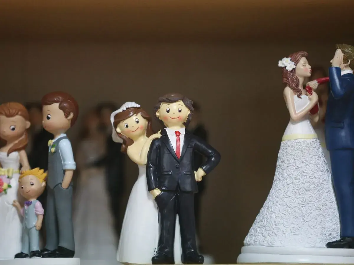 Figurines de couples mariés, certaines avec des enfants, sur un fond flou.