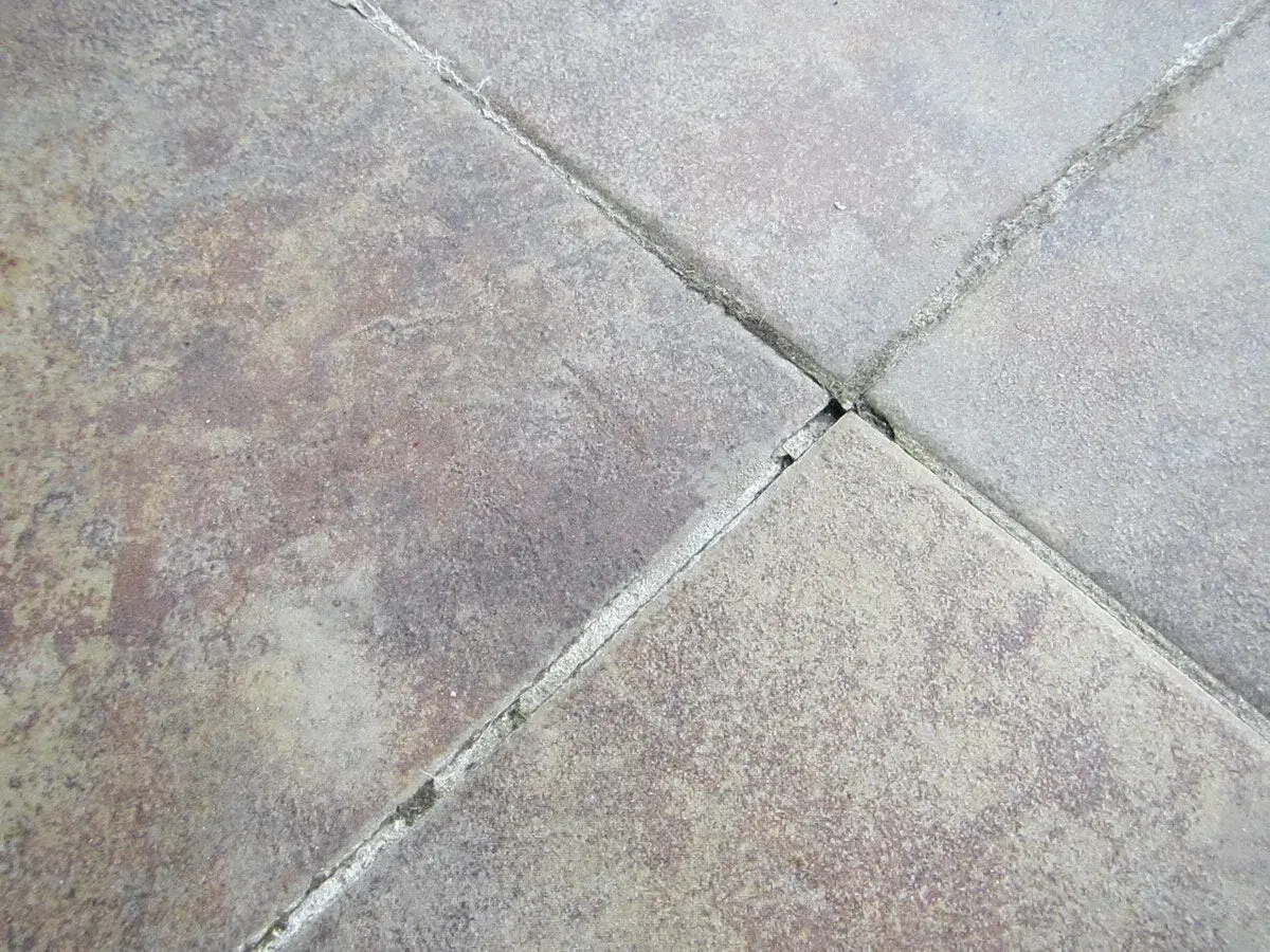 Close-up of weathered tiles showing significant tile grout cracking. The grout lines are broken and crumbling, indicating wear and tear.