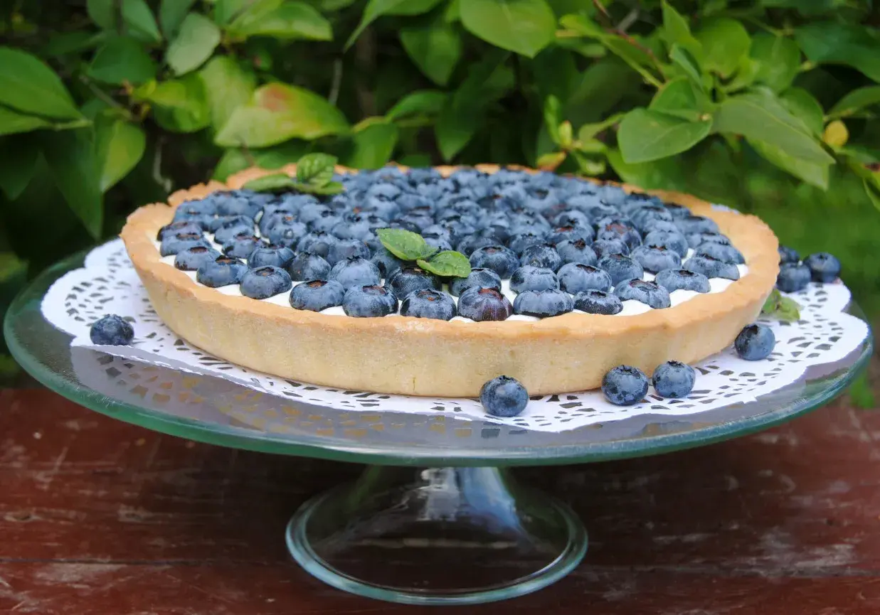 Pyszna tarta z borówkami, udekorowana listkami mięty, prezentuje się apetycznie na szklanej paterze.