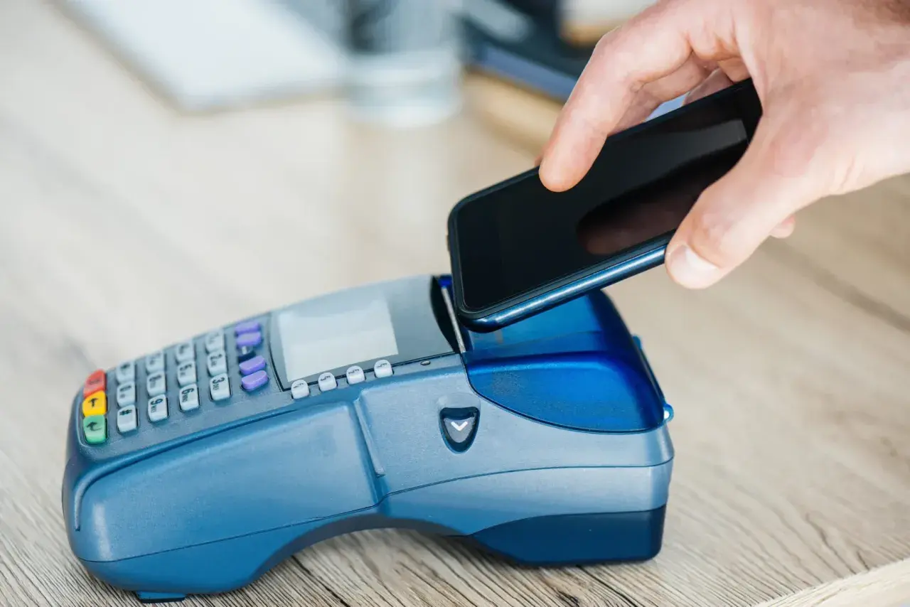 Dłoń zbliża smartfon do terminala płatniczego, realizując szybki booking paypo.