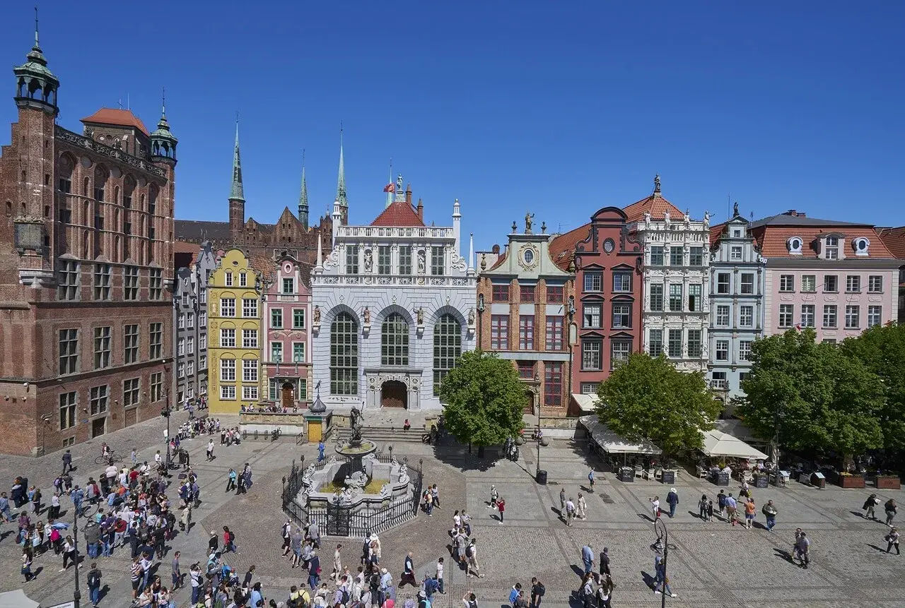 Tętniący życiem gdański plac z Dworem Artusa, fontanną Neptuna i kolorowymi kamieniczkami.