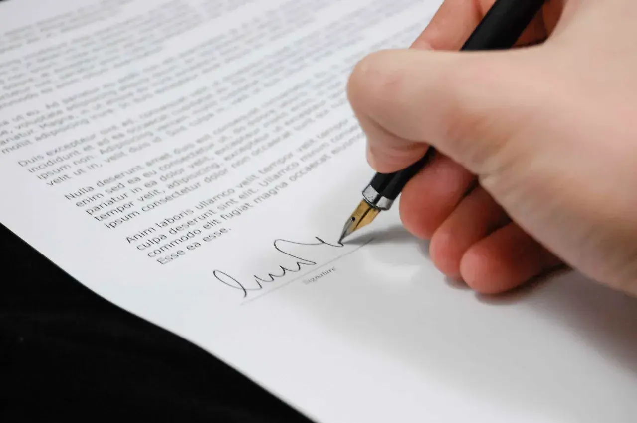 Mano firmando un documento con una pluma estilográfica, un paso clave para firmar contrato online.
