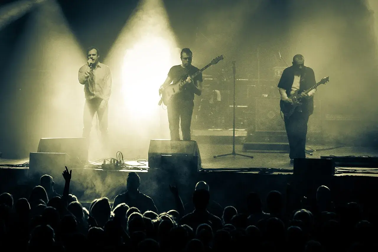 Koncert zespołu Coma z Leszkiem Żukowskim na wokalu. Muzycy na scenie, w tle dym i światła. Publiczność w pierwszym planie.