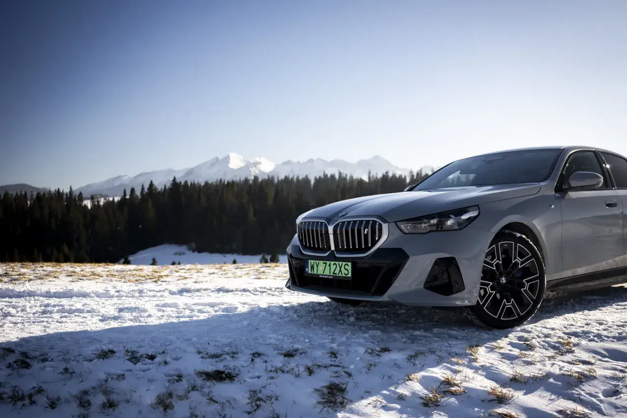 Szare BMW i5 na tle ośnieżonych gór i lasu.