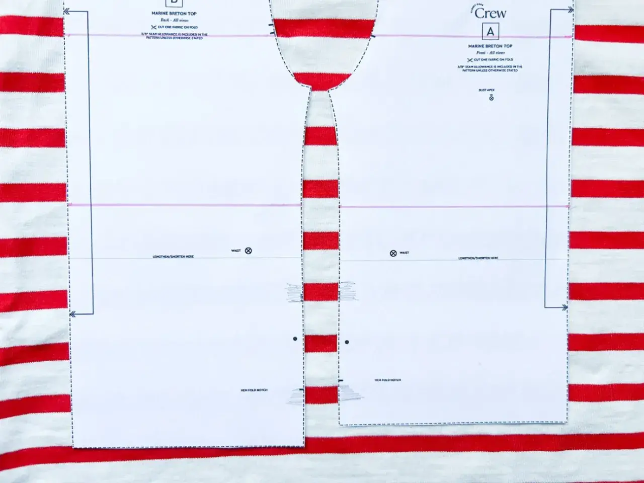 Wzór wykroju na bluzkę typu bretońskiego leży na materiale w biało-czerwone paski. Dzianina w paski idealnie pasuje do morskiego stylu.