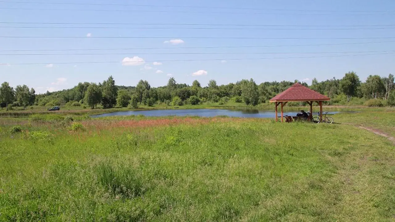 Malownicze jezioro krasowe otoczone zielenią, z altanką i rowerem przy brzegu.